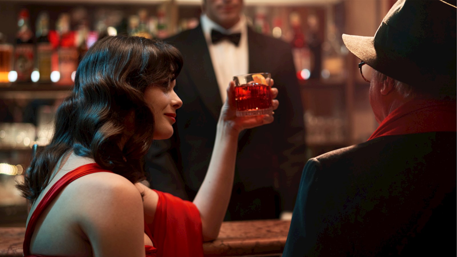 Woman in red dress sat at bar with a red drink